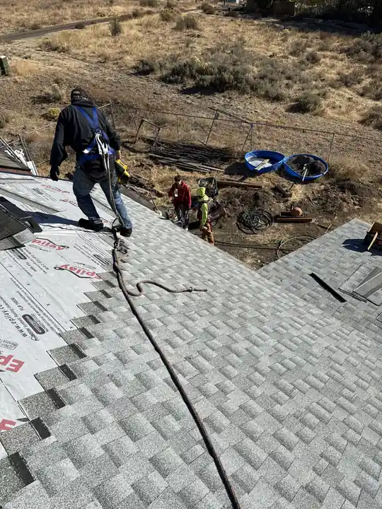 Crew laying architectural shingles over synthetic underlayment on a steep residential roof